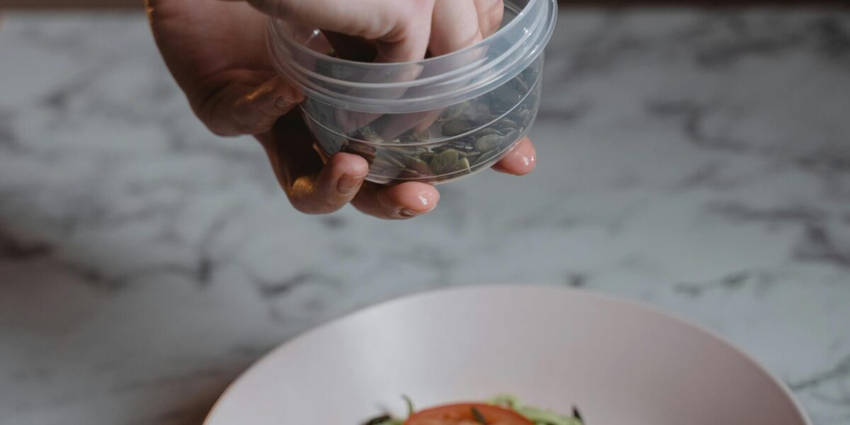 Person holding and using a plastic food container while preparing a healthy meal